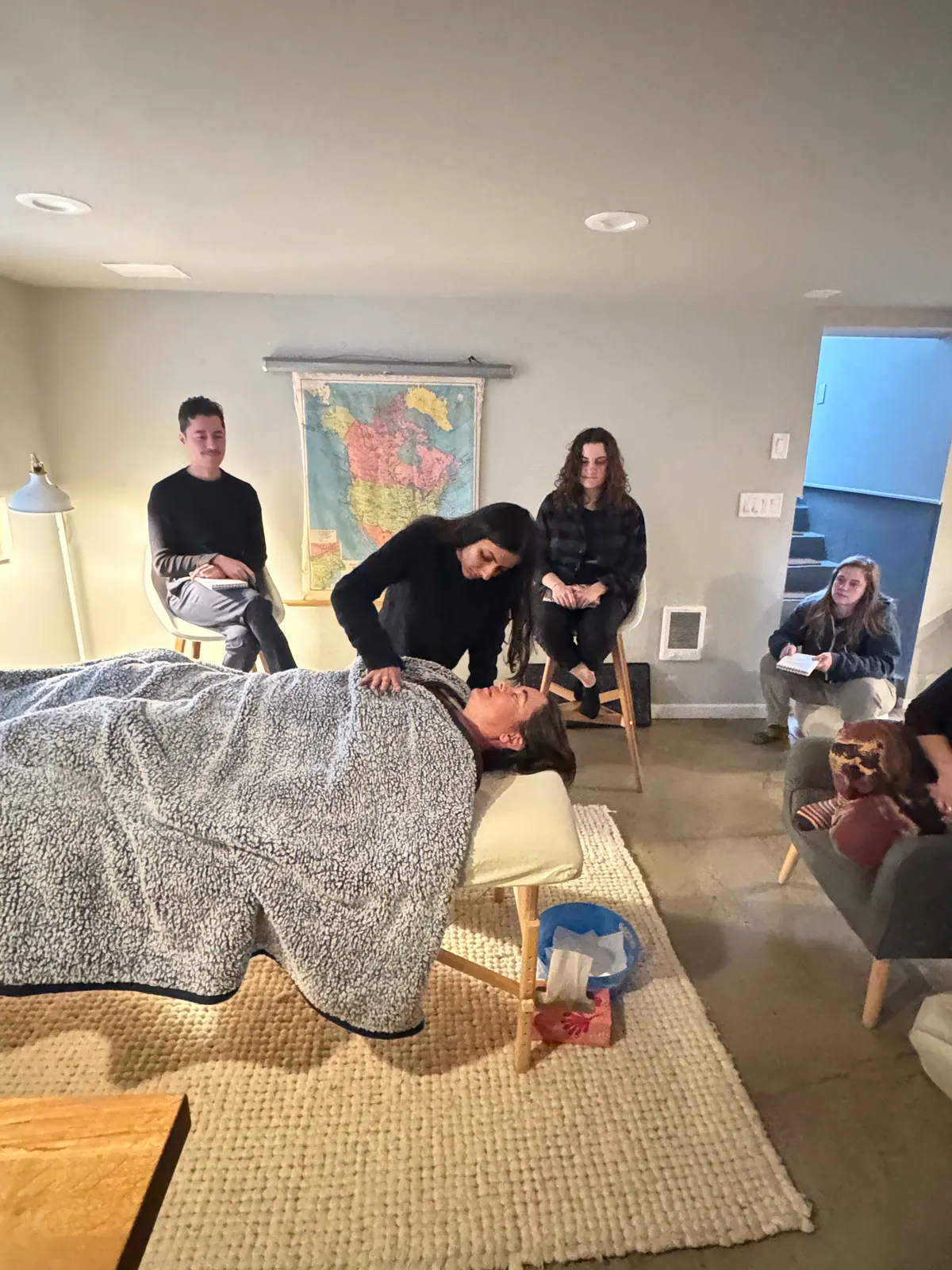 Practitioner working with a person lying on a table while a small group observes in a living room