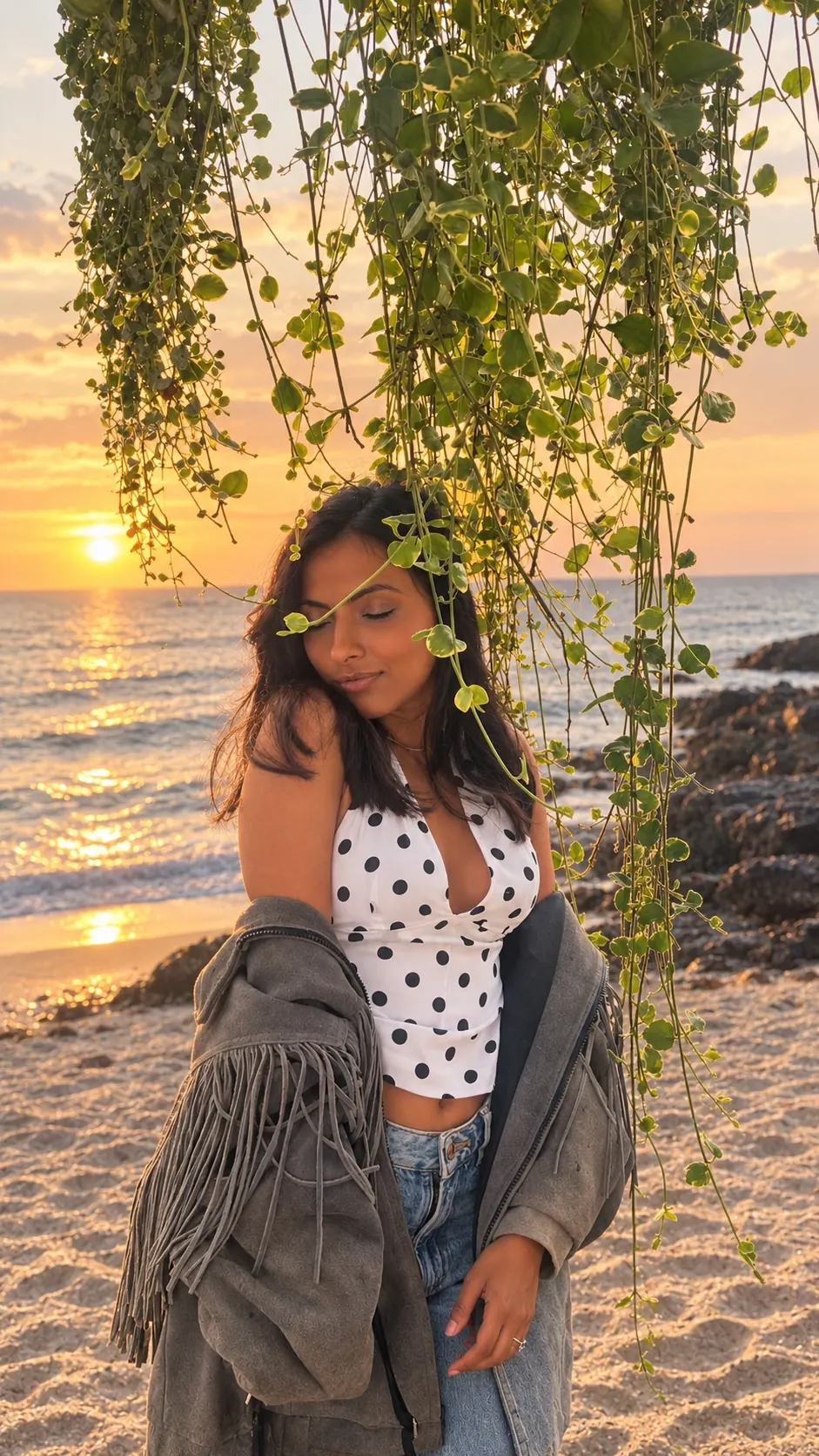 Woman with eyes closed on a beach at sunset beneath hanging green vines